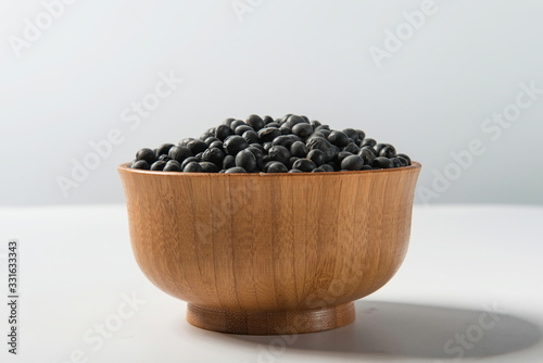 Tile (top view) black gram (Wigner mungo) on a wooden spoon under a straw mat on a white background.