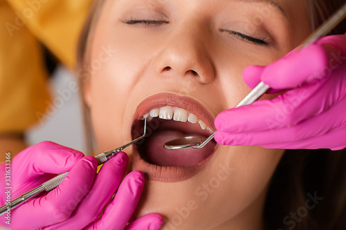 Beautiful blonde patient at the dentist. The young women's teeth being checked, examined and treated by a female dentist with the help of special medical tools