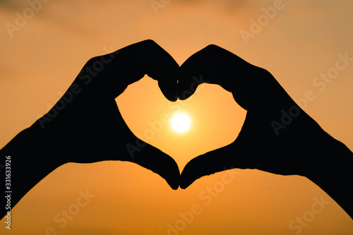 Silhouette hand in heart shape with sunrise on the sky background. love concept.