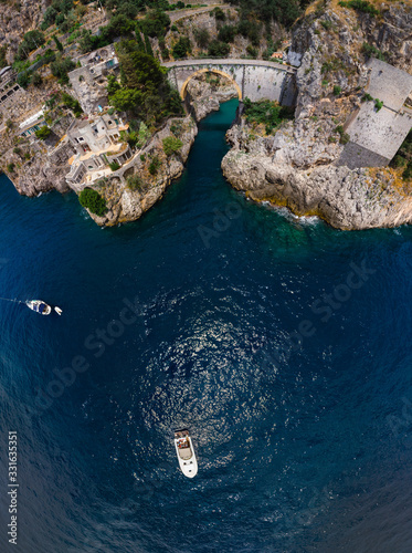Aerial top down view of stone bridge and clear blue water, Incredible beauty panorama. The rocky seashore of southern Italy. Boats with tourist. Fiordo di furore beach Amalfi coast.