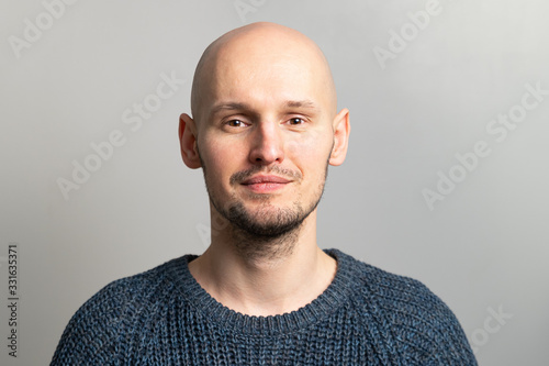 portrait of a young bald man in a knitted sweater on a gray background photo