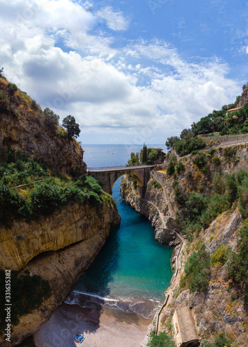 Vertical photo. Bay of Fiordo di furore beach. Incredible beauty panorama of a mountains paradise. The rocky seashore of southern Italy. Sunny day. Stone bridge and clear water. Amalfi coast.