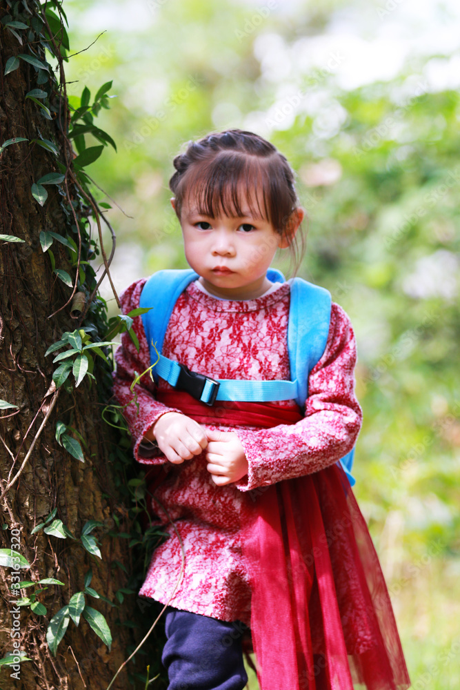 A little girl playing happily against a tree trunk A little girl playing happily against a tree trunk