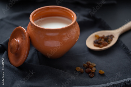 Brown pot with sour cream and a wooden spoon with raisins on a dark background.