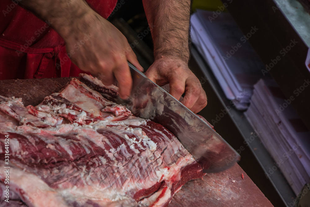 butcher cutting raw meat with knife in shop