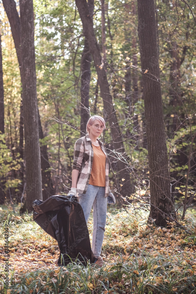 A young girl - an eco activist collects trash and plastic in a park and forest stacks up in a black big bag. Clean eco system concept A young girl - an eco activist collects trash and plastic in a park and forest stacks up in a black big bag. Clean eco system concept