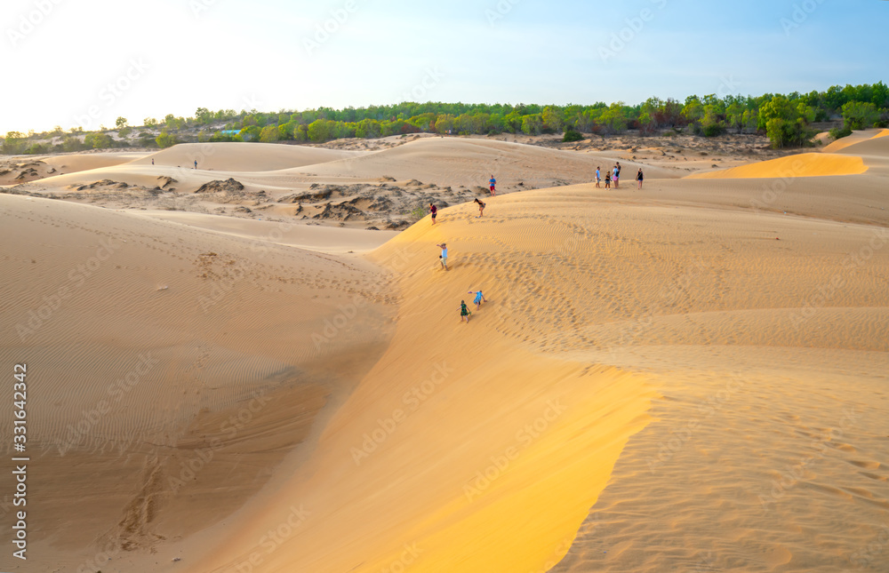 Foreign tourists experiencing the high golden sand hill to watch the sunset on top of desert in summer in Mui Ne, Vietnam