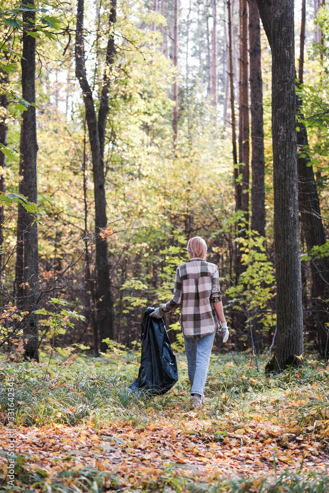 A young woman - an eco activist collects trash and plastic in a park and forest stacks up in a black big bag. Clean eco system concept A young woman - an eco activist collects trash and plastic in a park and forest stacks up in a black big bag. Clean eco system concept