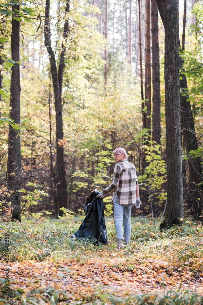 A young girl - an eco activist collects trash and plastic in a park and forest stacks up in a black big bag. Clean eco system concept