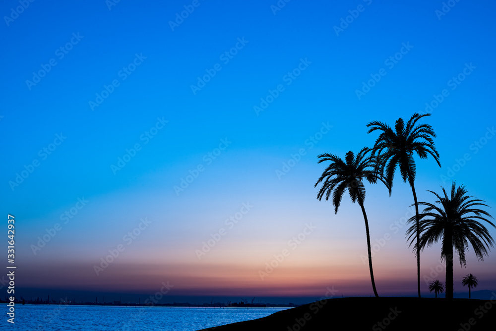 Sunset over the tropical sea with silhouettes of palm trees on the islets.