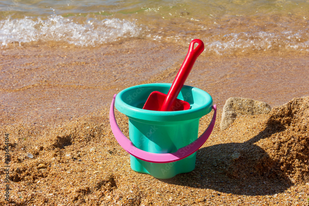 plastic children's toy bucket with a scoop on the sandy shore of the sea beach on a sunny summer day plastic children's toy bucket with a scoop on the sandy shore of the sea beach on a sunny summer day