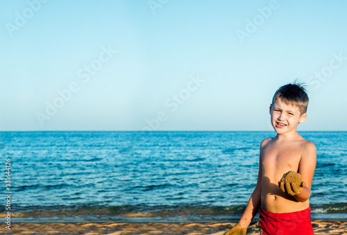 Sea holidays. Cute boy on the beach plays with sand. Casts a sand castle and cakes. sunset  blue sky and relax travel concept.copy space