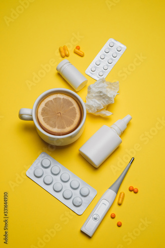 Pills, medical thermometer, nose spray, lemon tea. Different medications on yellow background. Cold and flu home remedies. Disease self-treatment concept. Flat lay. Vertical.