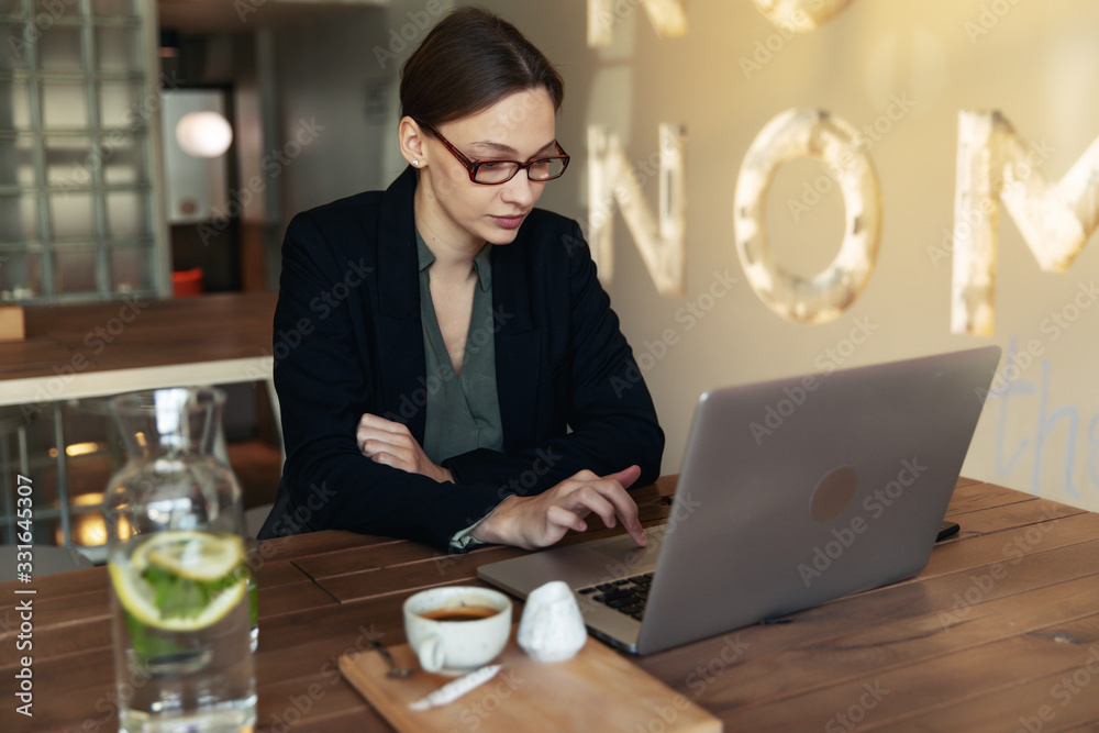 Focused business woman in stylish glasses sit on cafe working on laptop, concentrated serious female working with computer Focused business woman in stylish glasses sit on cafe working on laptop, concentrated serious female working with computer