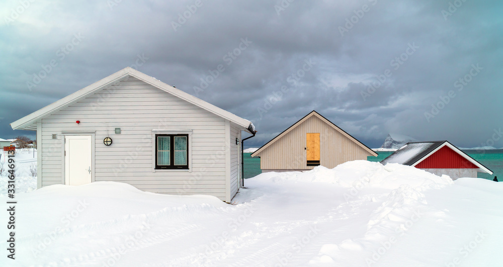 Sommarøy, Tromsø / Norway - March 6th, 2020: Three traditional wooden houses under the snow and a cloudy sky at Sommarøya Island in winter Sommarøy, Tromsø / Norway - March 6th, 2020: Three traditional wooden houses under the snow and a cloudy sky at Sommarøya Island in winter