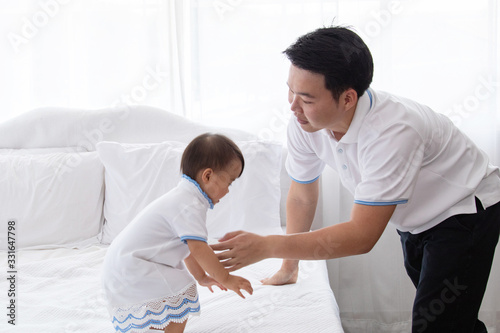 Asian young family help together feeding adorable cute girl at home, father playing with daughter hold her to fly on bed, mother pregnancy looking beloved husband and daughter multi task concept