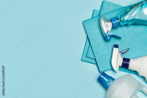 Productos de limpieza: botellas, aerosoles, pulverizador, paño esponja sobre fondo celeste pastel. Vista superior. Copy space