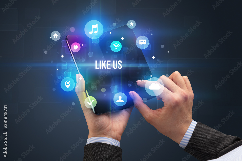 Businessman holding a foldable smartphone with LIKE US inscription, social media concept Businessman holding a foldable smartphone with LIKE US inscription, social media concept