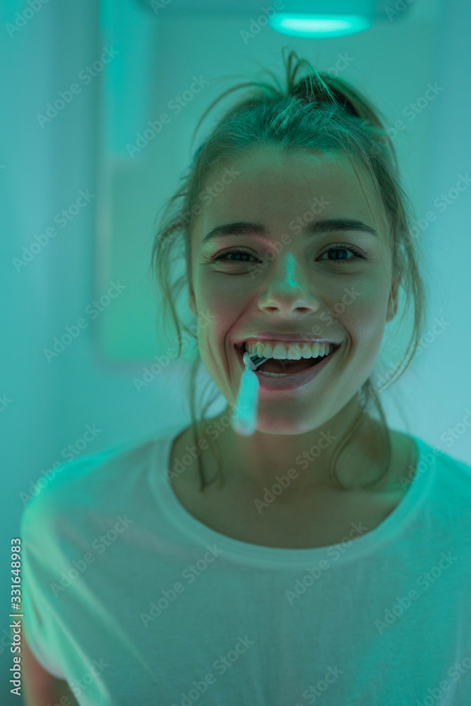 Pleasant funny young girl brush her teeth, use toothbrush at bathroom for healthy tooth with happy. Smiley female in her bathroom. Blue and green neon background. Pleasant funny young girl brush her teeth, use toothbrush at bathroom for healthy tooth with happy. Smiley female in her bathroom. Blue and green neon background.