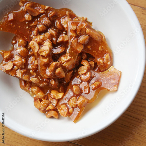 Peanut brittle pieces on a white bowl on wooden table