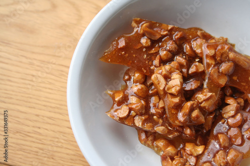 Peanut brittle pieces on a white bowl on wooden table photo