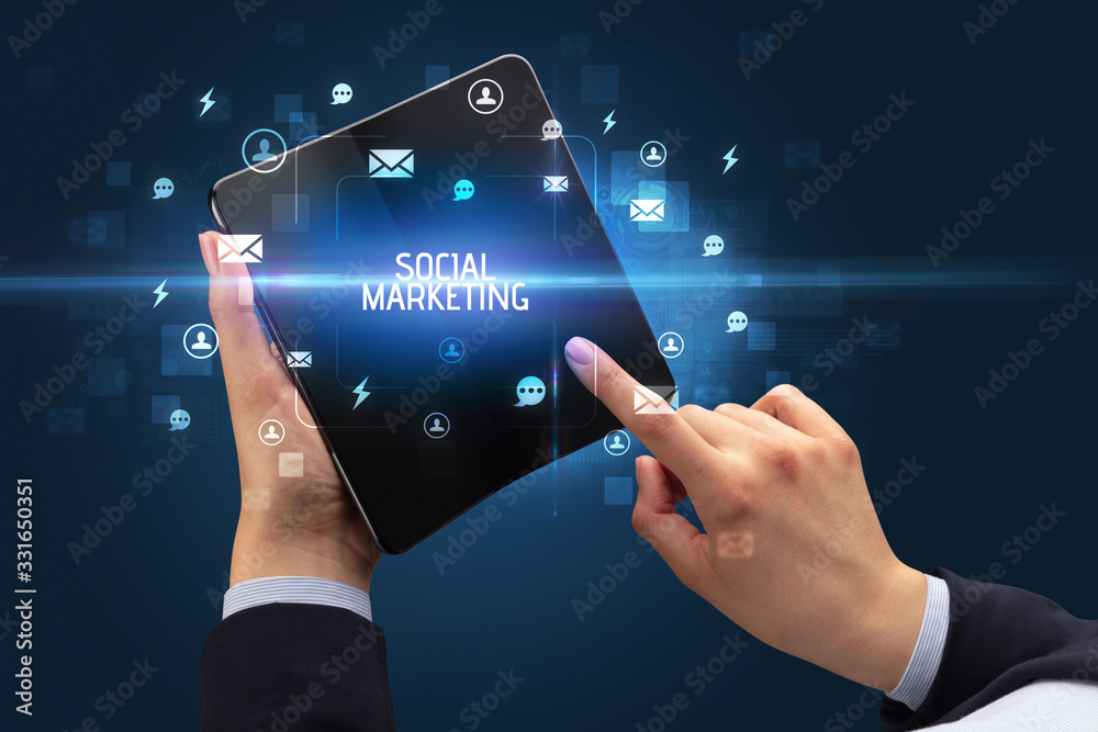 Businessman holding a foldable smartphone with SOCIAL MARKETING inscription, social networking concept Businessman holding a foldable smartphone with SOCIAL MARKETING inscription, social networking concept