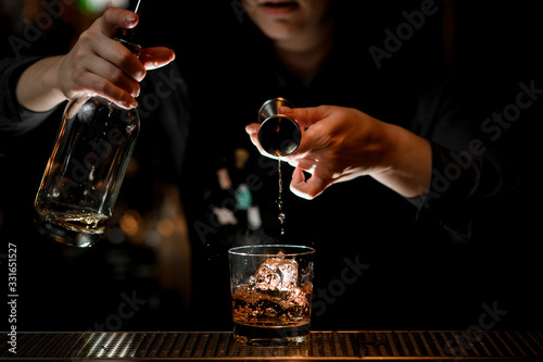 bartender elegantly pours alcoholic drink to glass with ice using beaker