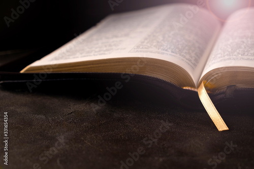 Open Bible on a dark table with light coming from above. Christianity concept. Holy Bible background.
