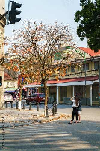 Hanoi street in autumn with yellow leave tree and people taking photo on old town street