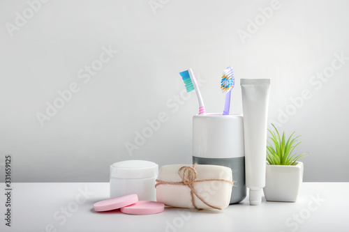 Toothbrushes in cup, toothpaste and other toiletries on grey background photo