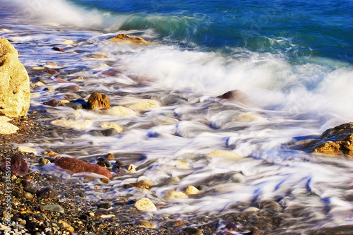 Sea pebbles in coastal sea waves. The shore plays with paints in the sunlight.