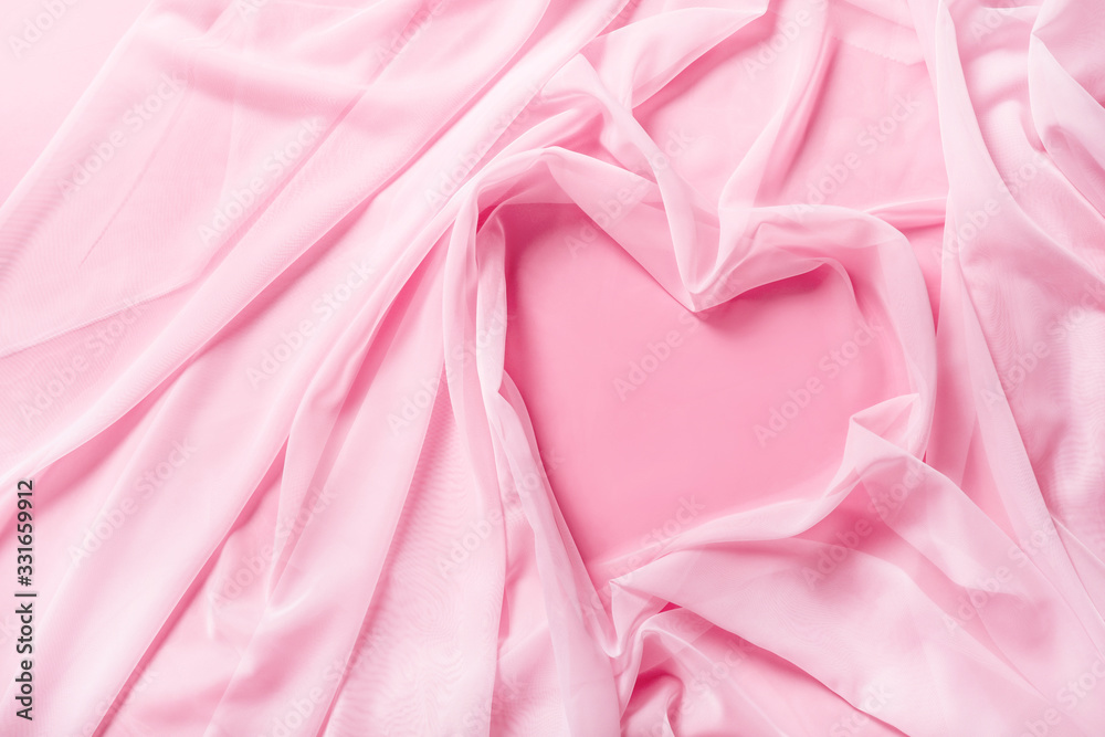 Tender pink silk fabric draped in shape of heart in pink background