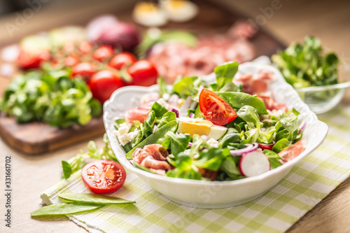 Fresh spring salad with green leaves tomatoes egg radish red onion young peas prosciutto feta cheese and olive oil