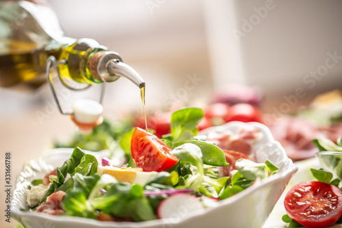 Bottle with olive oil pouring into salad