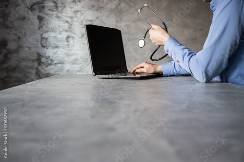 Lekarz ze stetoskopem w dłoni przed komputerem na betonowym tle