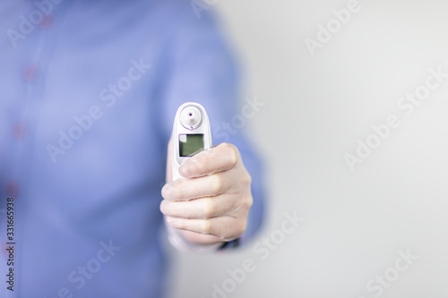 Lekarz w niebieskiej koszuli na jasnym tle trzymający w dłoni termometr
