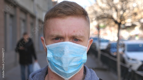Portrait of young man with medical face mask stands at city street. Guy wearing protective mask from virus outdoor in the people crowdy. Concept of health and safety life from coronavirus pandemic