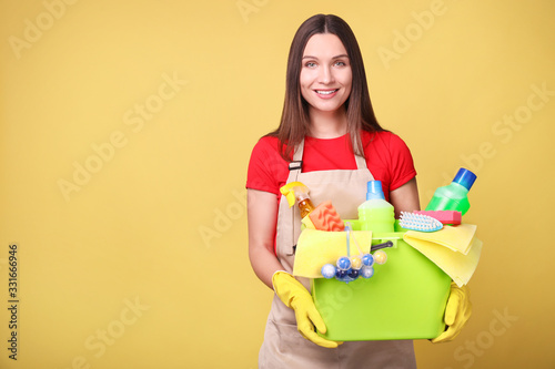 Young woman in apron on yellow background. Cleaning concept