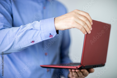 Mężczyzna w niebieskiej koszuli trzymający czerwony laptop w dłoniach na jasnym tle