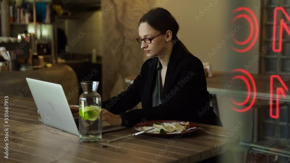 Focused business woman in stylish glasses sit on cafe working on laptop, concentrated serious female working with computer and cappuccino in coffee shop, freelancer, studying online, browse internet, 