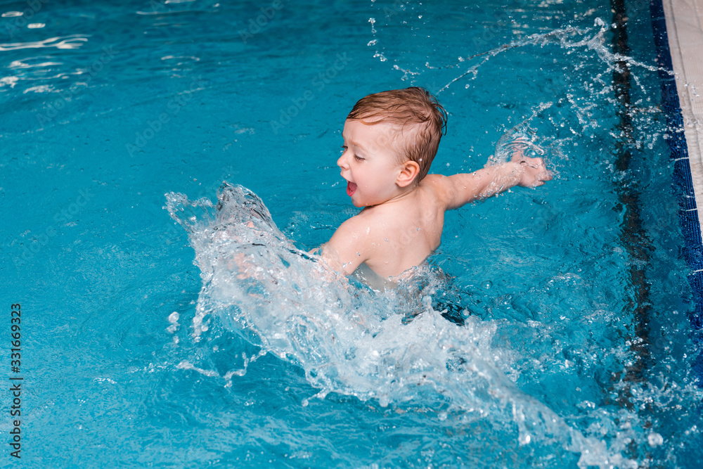 excited toddler boy splashing water in swimming pool