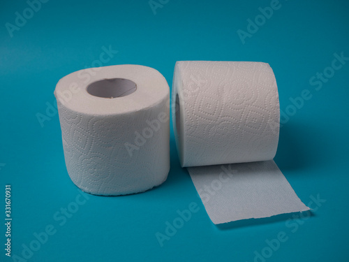 Two rolls of white perforated two-layer toilet paper isolated on a blue background close-up.