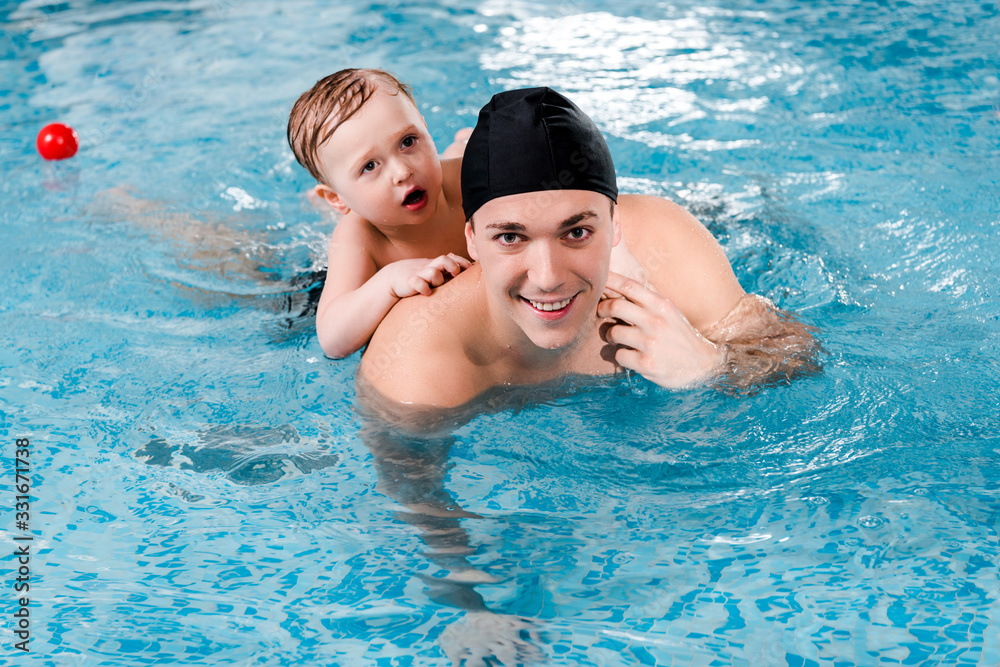 happy swim coach and toddler boy training in swimming pool