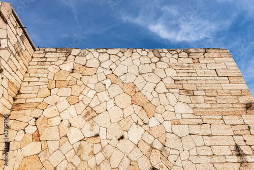 Closeup of an Austrian fortified wall made of irregular stone blocks on a blue sky with clouds