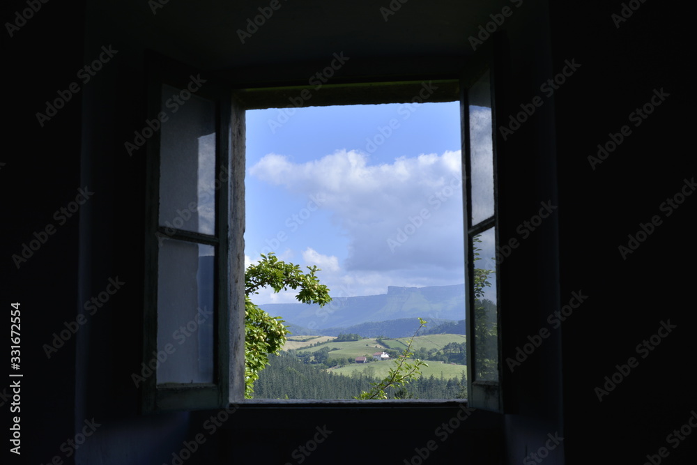 Paisaje verde con bosques y prados y la sierra en el horizonte visto desde el interior de una casa oscura a través de una vieja ventana