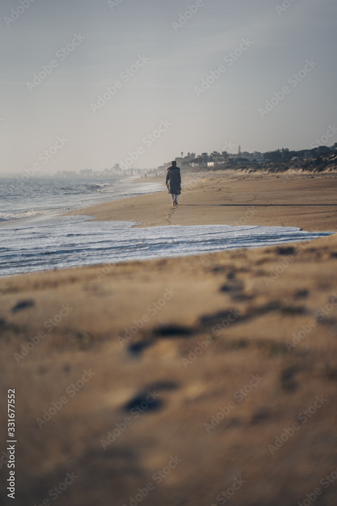 Beautiful woman walking on an empty beach in Portugal, leaving foot steps behind