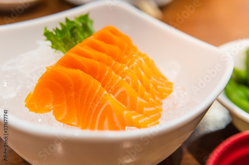 Partly focused of salmon sashimi dish serving on ice to preserve the freshness. Picture is included the artificial light.