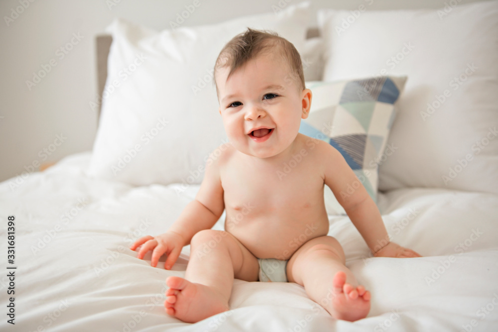 Cute baby girl sitting on the white bedding and smiling