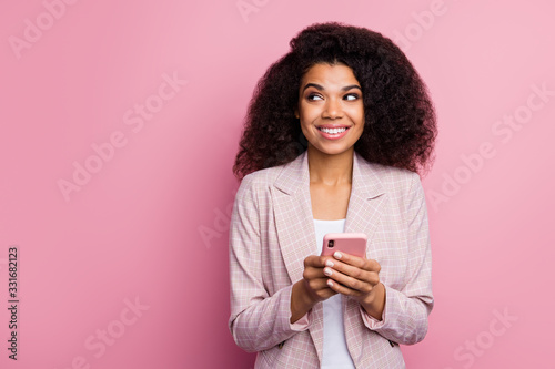 Photo of beautiful funny positive dark skin lady hold telephone hands look side empty space have interesting idea creative person wear plaid blazer isolated pastel color background