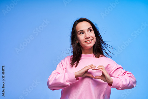 Young woman in pink dress showing heart with her hands on blue background photo